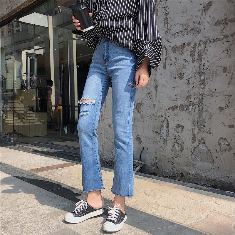 Woman with a striped shirt, ripped jeans, and black and white shoes holding a coffee cup