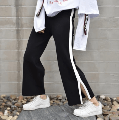 Woman wearing black pants, white sneakers, and a white top standing on a slab on top of stones