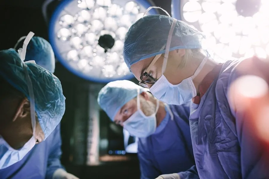 three surgeons working on a patient with lights in the background